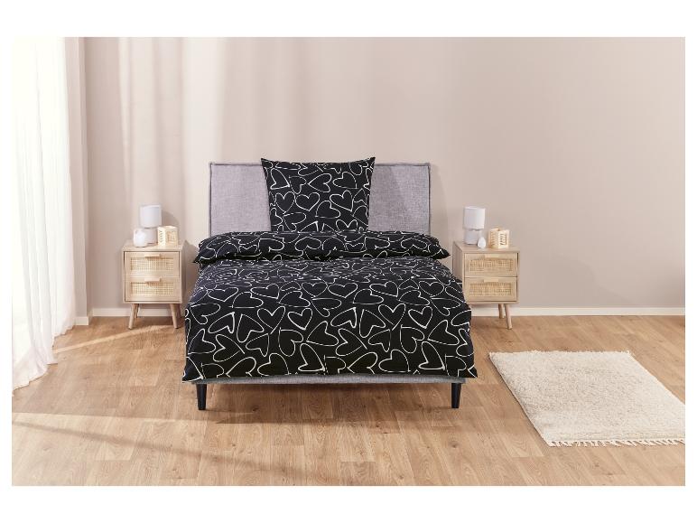 Ein schwarzer Bettbezug mit weißen Herzen auf einem Bett mit grauem Kopfteil.