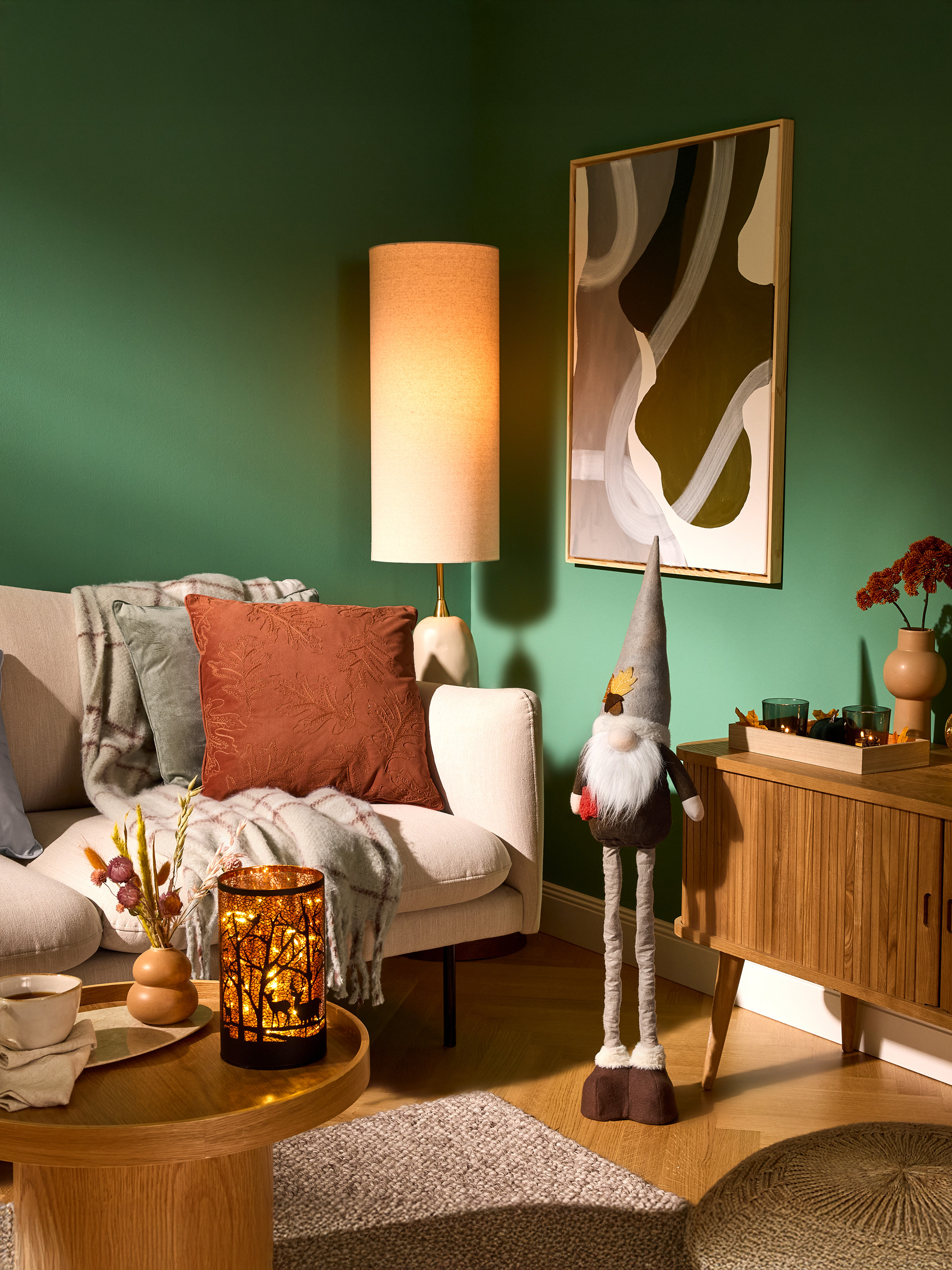 Gemütliches Wohnzimmer mit grünen Wänden, Sofa, Stehlampe und Herbstdekorationen.