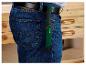 Mann in blauen Jeans und schwarzem Gürtel, der eine grüne Astsäge an der Seite trägt.
