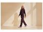 Frau in dunkelviolettem Hoodie und passender Jogginghose geht, mit Schatten an der Wand.