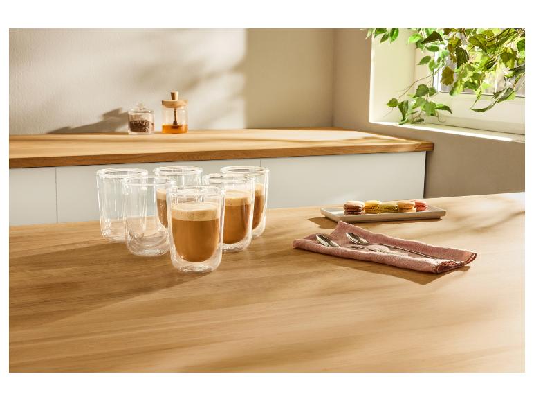 Kaffeetassen mit Kaffee und Macarons auf einem Holztisch in der Küche.