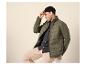 Mann in grüner Steppjacke, schwarzer Mütze und beiger Hose, lächelnd und nach rechts blickend.