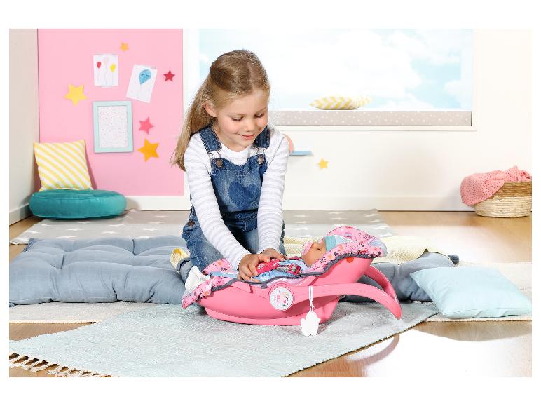 Mädchen spielt mit einer BABY born Puppe in einem rosa Autositz auf einem Teppich im Kinderzimmer.