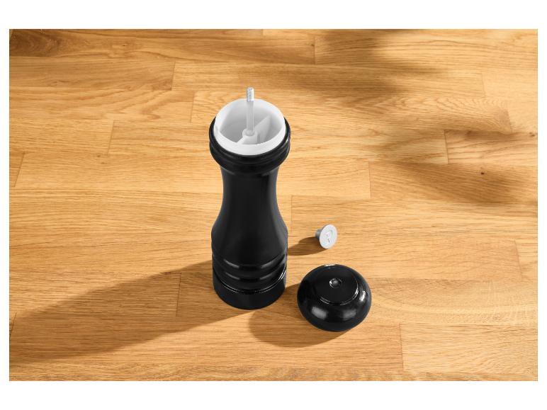 Schwarze Pfeffermühle mit Deckel und 'P'-Markierung auf einem Holztisch.