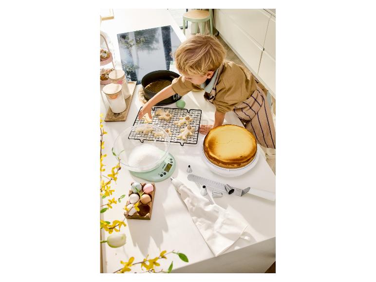 Kind dekoriert Kekse und einen Käsekuchen auf einer Küchenarbeitsplatte mit Backutensilien.