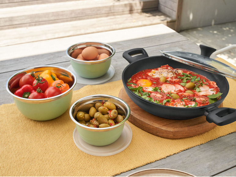 Eine Pfanne mit Spiegeleiern, Tomaten und Oliven, zusammen mit Schüsseln mit Oliven und anderen Zutaten.