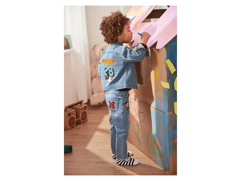 Kind in Mickey Mouse Jeans und Jeansjacke bemalt ein Kartonhaus.
