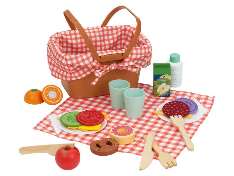Picknick-Set mit Korb, karierter Decke, Sandwiches, Obst, Getränken und Besteck.