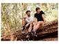 Paar in Sport-T-Shirts und Schuhen sitzt auf einem Baumstamm im Wald.