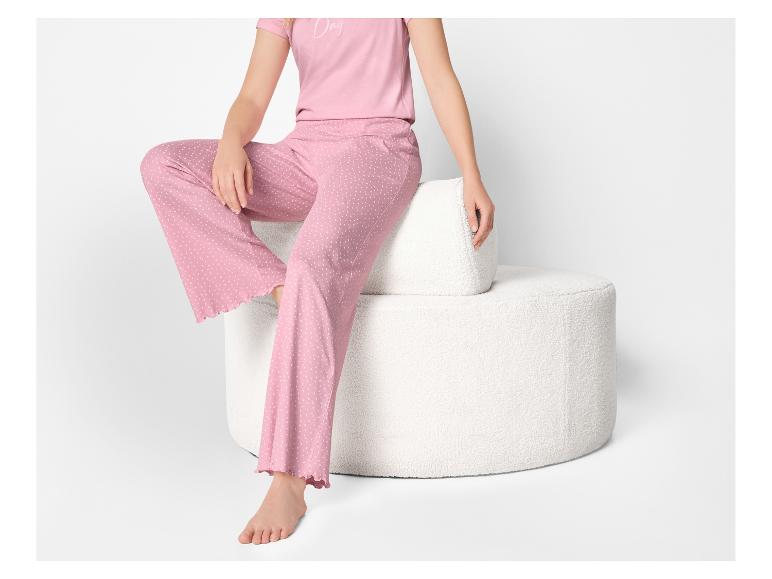 Frau in rosa gepunktetem Pyjama, sitzend auf einem weißen strukturierten Hocker.