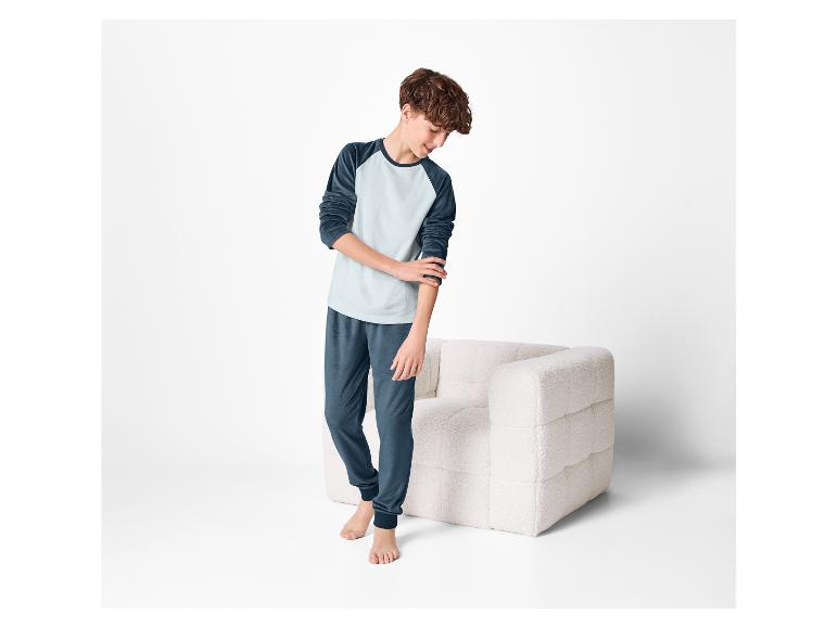 Ein Junge in bequemen Pyjamas, der neben einem weichen Sessel steht.