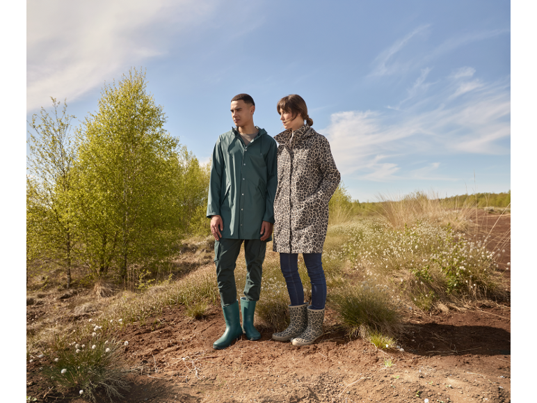 Mann und Frau in Regenjacken und Stiefeln stehen in der Natur.