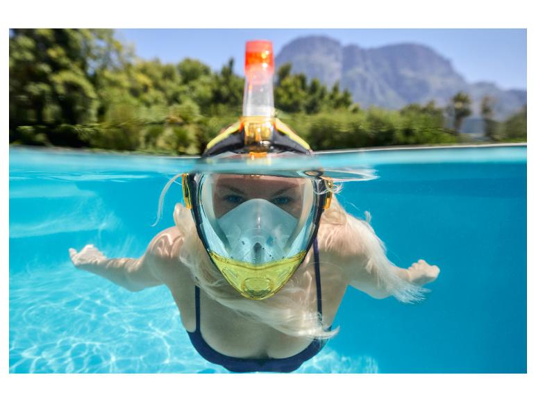 Frau mit Schnorchelmaske und Schnorchel schwimmt in einem Pool, mit Bergen und Bäumen im Hintergrund.