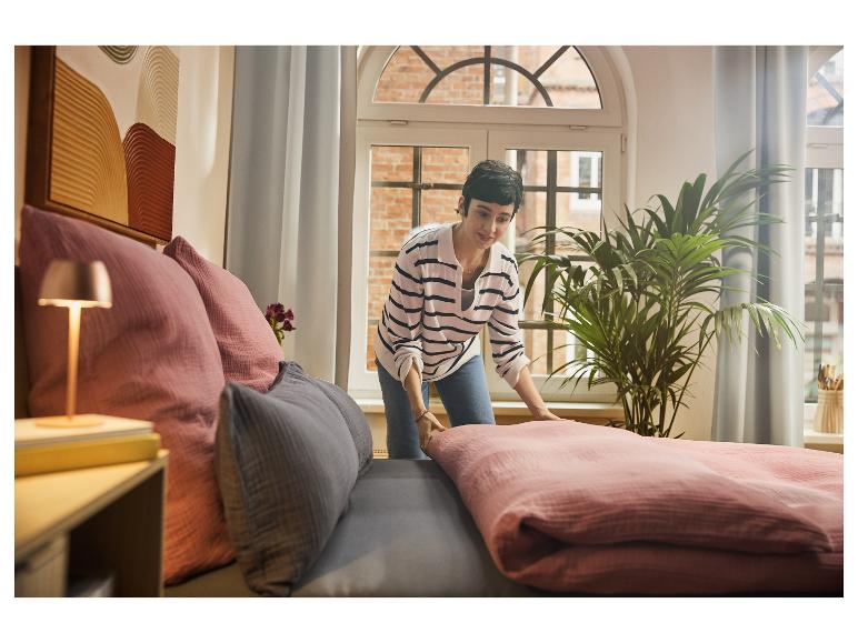 Frau macht Bett mit rosa Bettwäsche und grauen und rosa Kissen.