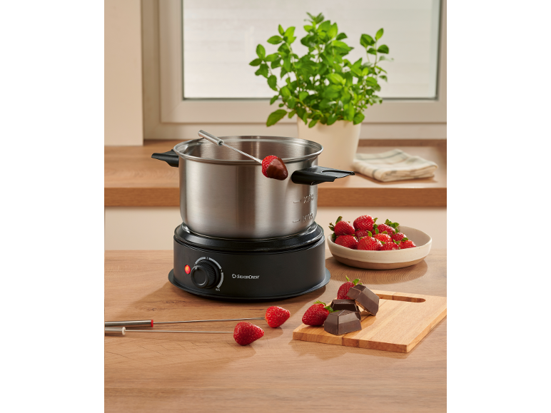 Schokoladenfondue-Set mit Erdbeeren und Schokoladenstücken auf einem Holztisch.