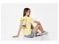 Frau in gelbem T-Shirt mit „Ciao Bella“-Aufdruck und Jeans-Shorts, auf dem Boden sitzend.