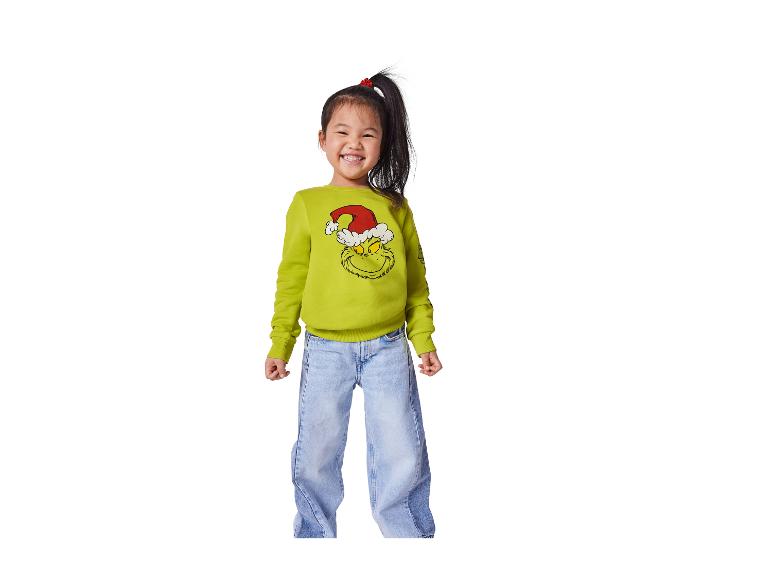 Lächelndes Mädchen in grünem Grinch-Pullover und blauen Jeans.