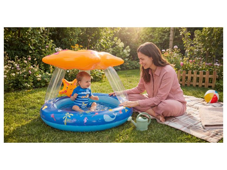 Frau und Baby spielen in einem aufblasbaren Pool mit Sonnenschutz im Garten.