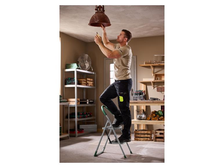 Mann auf Leiter wechselt Glühbirne in Deckenlampe in Werkstatt.