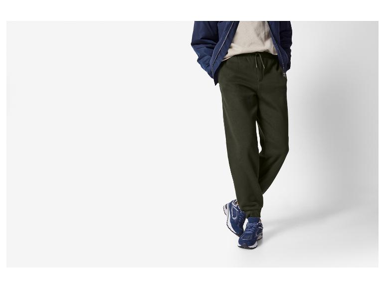 Person trägt grüne Jogginghose, eine blaue Jacke und blaue Sneaker.