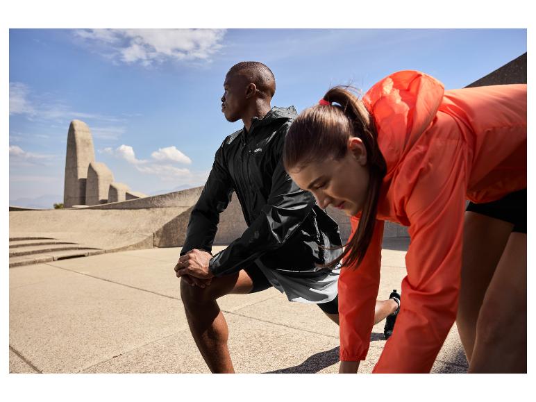 Zwei Sportler in Sportkleidung dehnen sich draußen, mit einem Denkmal im Hintergrund.