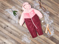 Ein rosa-roter Winteroverall für Babys auf einem Holzboden mit Schnee.