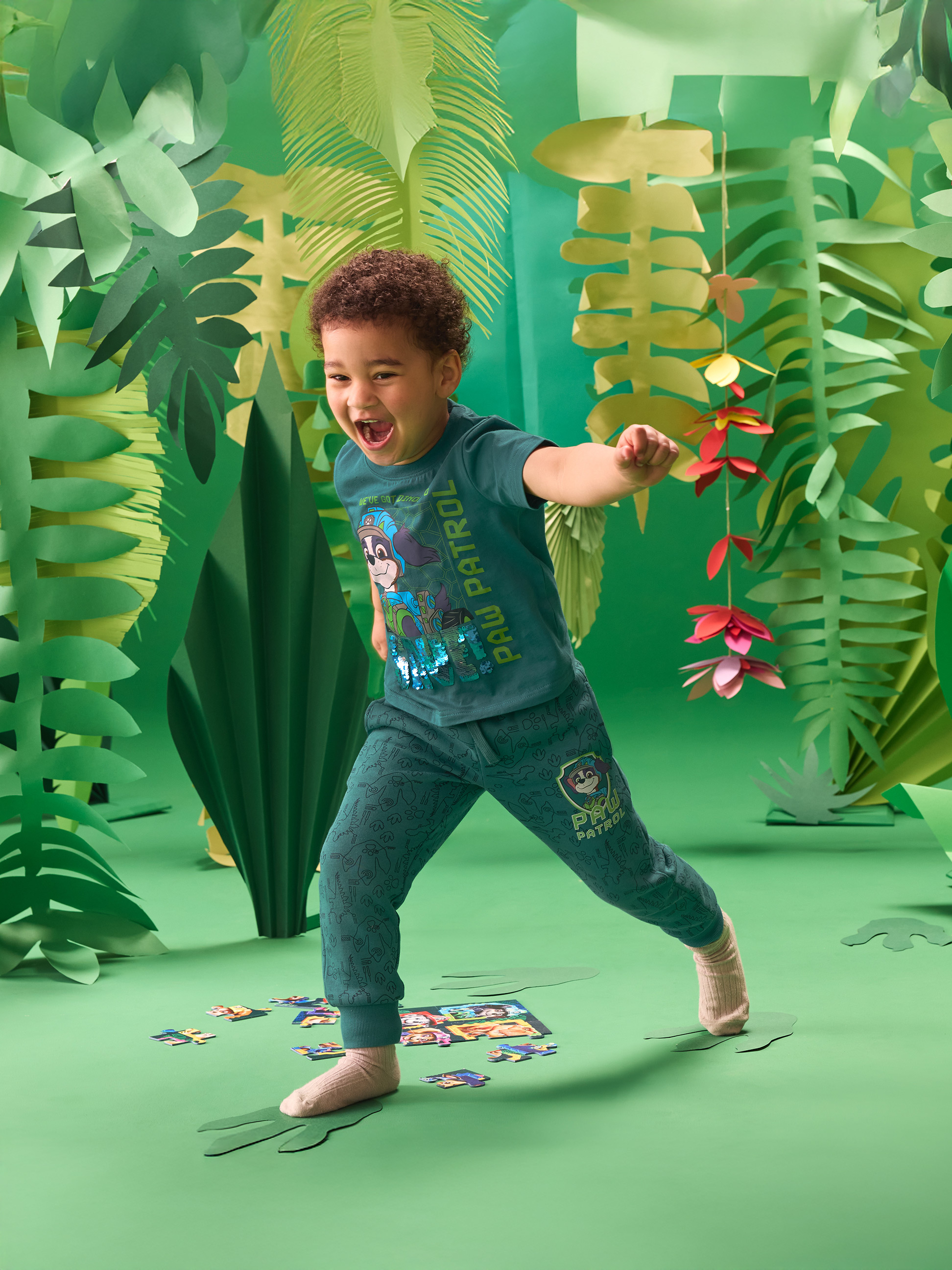 Kleinkind in grünem Dschungel-T-Shirt und Jogginghose, spielt mit einem Puzzle.