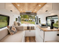 Wohnmobil-Interieur mit Küchenbereich, Sofa und Bett, mit Blick auf See und Zelte.