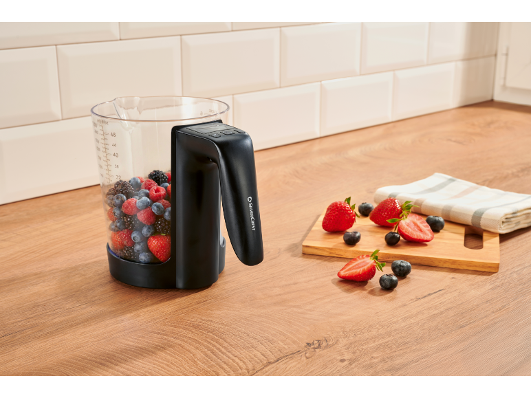 Mixerkrug gefüllt mit Beeren auf einer Küchenarbeitsplatte, mit geschnittenen Erdbeeren daneben.