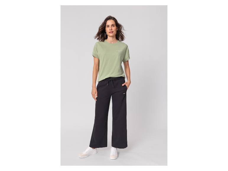 Frau in hellgrünem T-Shirt mit Text und schwarzer weiter Hose.