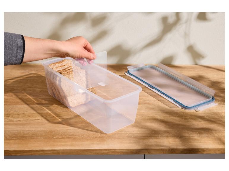 Hand hält einen transparenten Lebensmittelbehälter mit Brot und Deckel auf einem Holztisch.