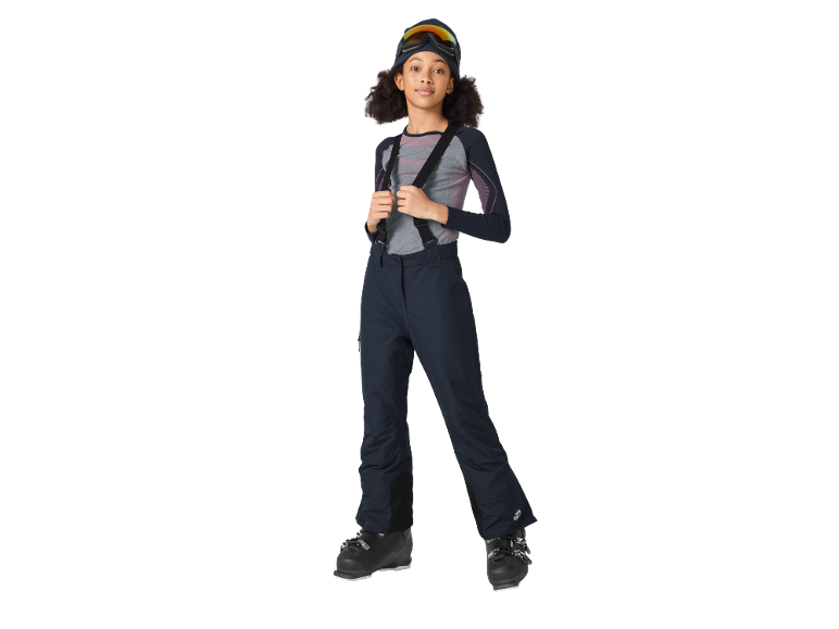 Mädchen in Skiausrüstung: Thermoshirt, Skihose mit Hosenträgern, Skibrille und Skischuhe.