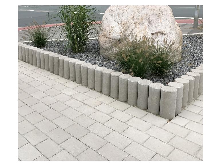 Beton-Gartenumrandung mit Zierpflanzen und einem großen Felsen.