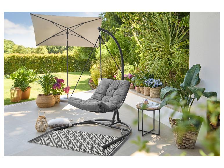 Außenterrasse mit grauem Hängesessel, Sonnenschirm, Pflanzen und gemustertem Teppich.