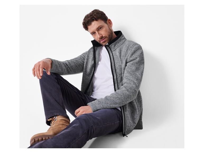 Mann in grauer Fleecejacke, weißem T-Shirt und dunkler Jeans.