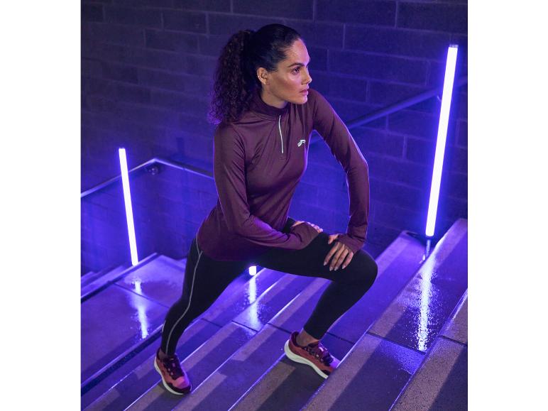 Eine Frau in Reebok Sportbekleidung, darunter ein lila Oberteil und schwarze Leggings, trainiert auf einer Treppe.