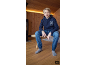 Junge in dunkelblauem Kapuzenpullover und Jeans sitzt auf einer Holzbank.
