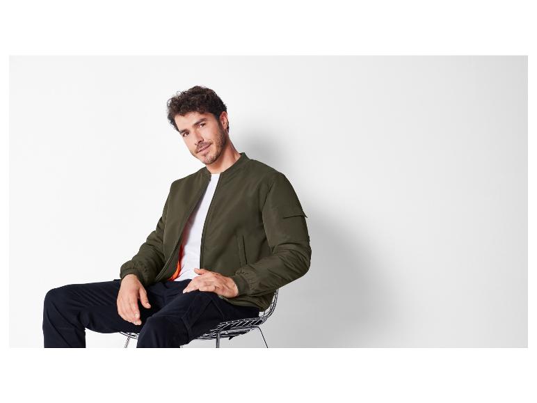 Mann in einer grünen Bomberjacke und schwarzen Hosen.