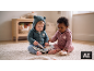 Zwei Babys in Strickstramplern, eines liest ein Stoffbuch, das andere spielt mit einem Spielzeug.