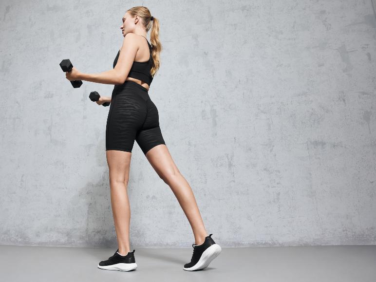 Frau in schwarzen Leggings und Sport-BH trainiert mit Hanteln.