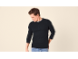 Mann in schwarzem Langarm-Henley-Shirt und Jeans, blickt nach unten.