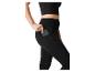 Frau in schwarzem Crop-Top und Leggings, steckt ein Telefon in die Seitentasche.