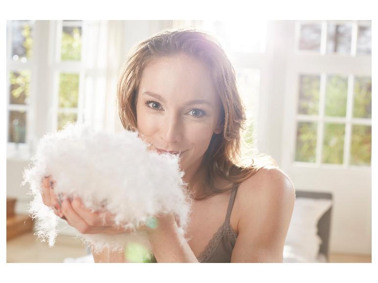 Frau hält flauschige Federn in den Händen und lächelt in die Kamera.