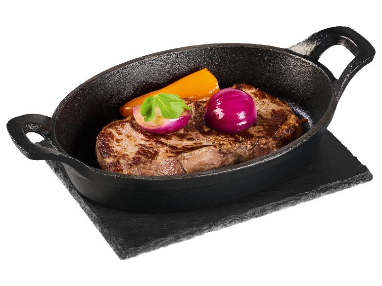 Rindersteak mit Rotzwiebel und Paprika in einer Gusseisenpfanne auf einem Steinbrett.