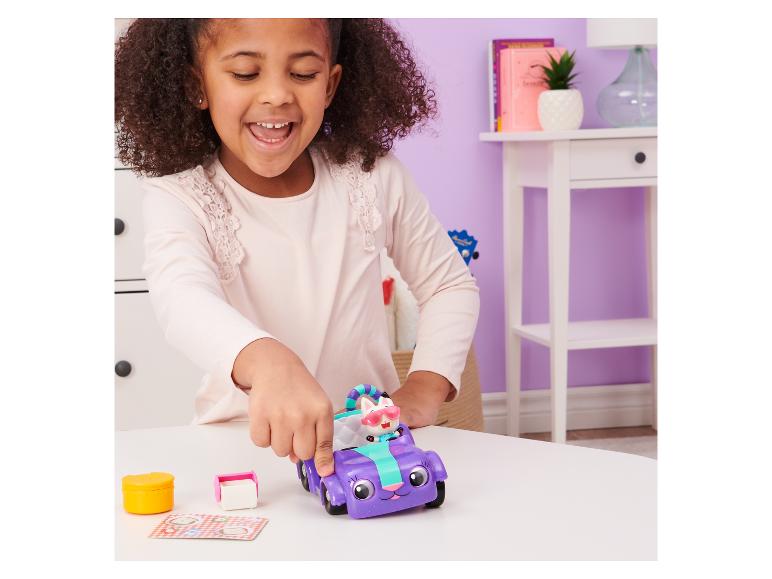 Ein Mädchen spielt mit einem lila Spielzeugfahrzeug und einer Katzenfigur auf einem Tisch.