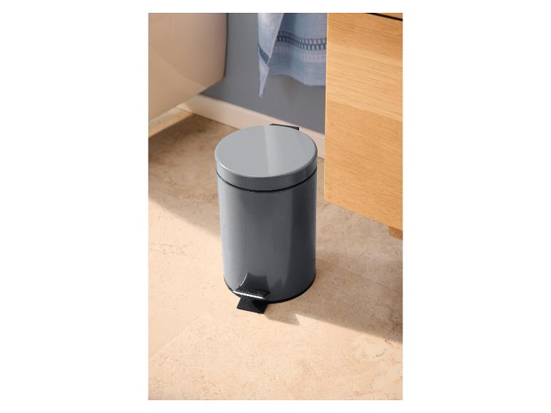 Grauer Treteimer in einem Badezimmer mit hellen Fliesen und einem Holzschrank.