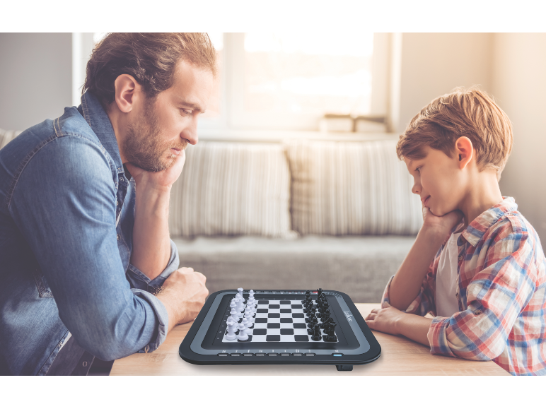 Vater und Sohn spielen an einem Holztisch auf einem elektronischen Schachbrett.