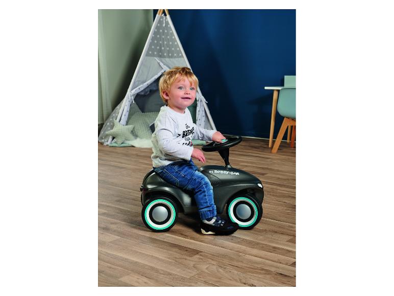 Kleinkind fährt ein Rutschauto in einem Zimmer mit Spielzelt.