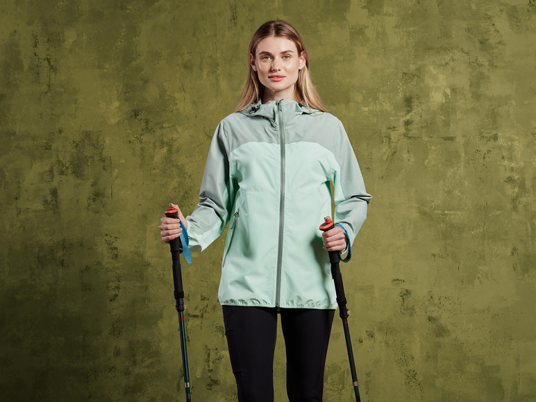 Eine Frau in einer grünen Jacke mit Wanderstöcken.