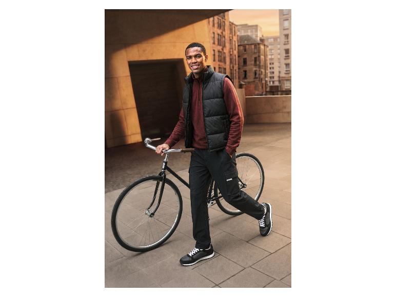 Mann mit Fahrrad, trägt eine Steppweste, Pullover und Cargohose.